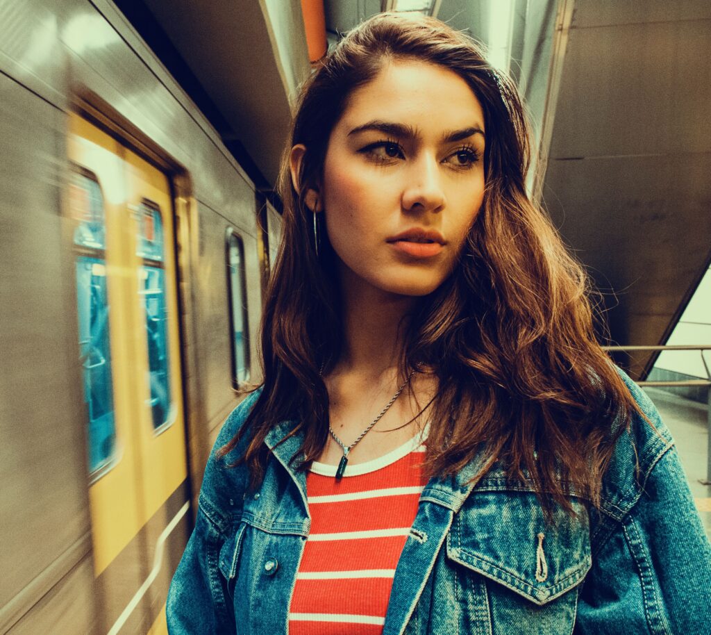 Portrait of a young woman in denim jacket with striped shirt at an urban subway station.